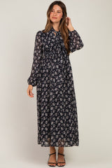 woman wearing a floral black maternity maxi dress with long sleeves and a tied neckline, showing her baby bump