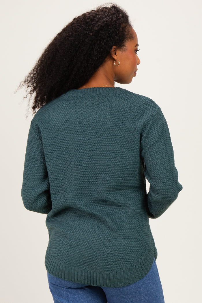 woman wearing a dark teal textured sweater, standing with her back to the camera, paired with blue jeans