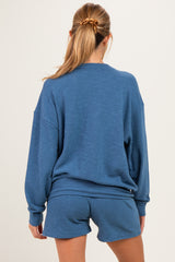 woman wearing a blue maternity sweatshirt and matching shorts, showing a relaxed fit from the back