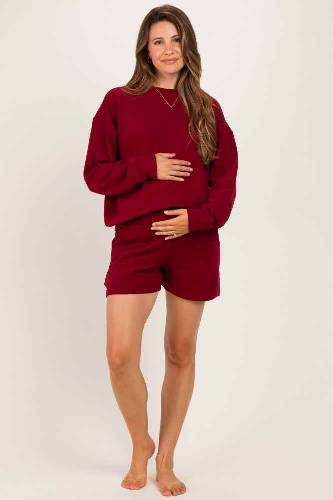 woman wearing a burgundy maternity sweatshirt and shorts, holding her baby bump