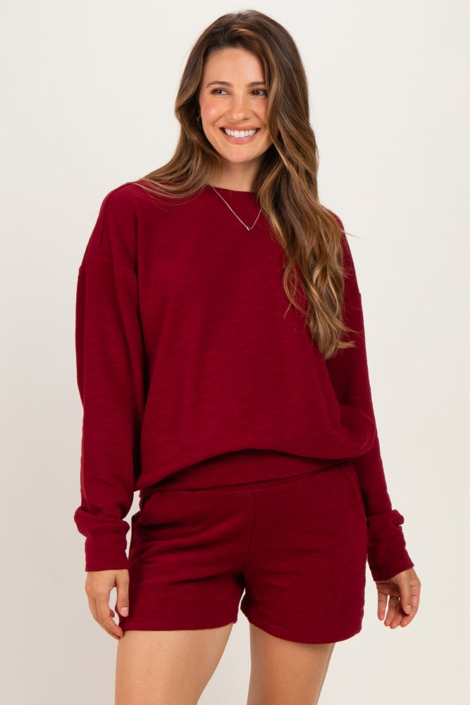 woman wearing a maroon maternity sweatshirt and matching shorts, smiling and styled casually