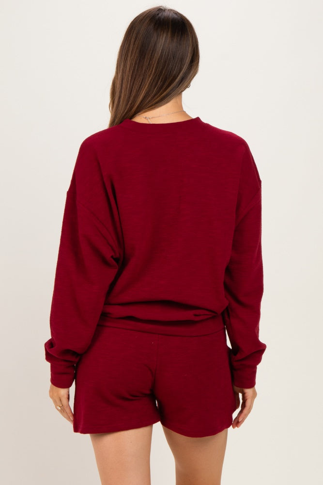 woman wearing a burgundy maternity loungewear set with a long sleeve top and shorts, showing her back and relaxed fit
