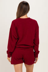 woman wearing a burgundy maternity loungewear set with a long sleeve top and shorts, showing her back and relaxed fit
