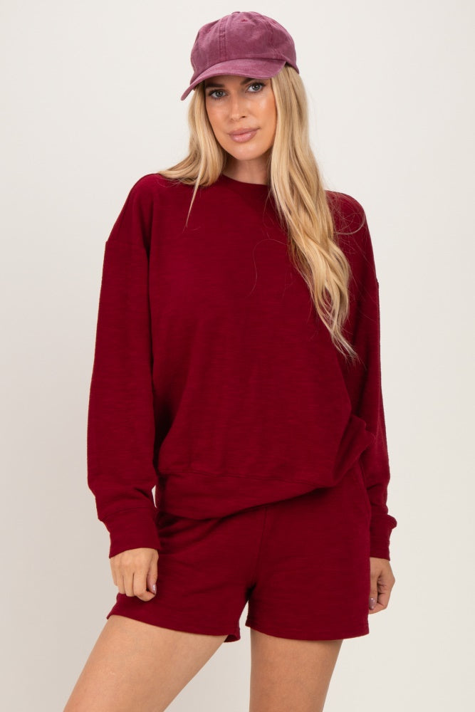 woman wearing a burgundy long sleeve sweatshirt and matching shorts, accessorized with a burgundy cap