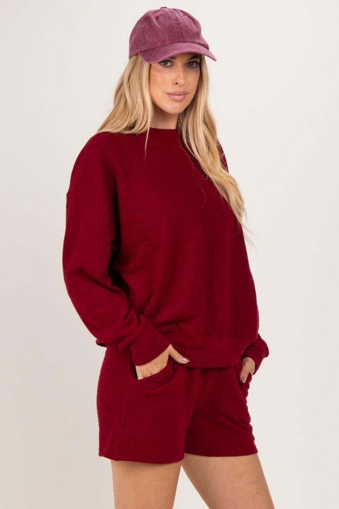 woman wearing a burgundy oversized sweater and matching shorts, styled with a purple cap