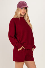 woman wearing a burgundy oversized sweater and matching shorts, styled with a purple cap