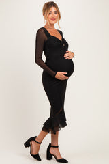 woman wearing a black maternity dress with long sheer sleeves and a ruffled hem, showcasing her baby bump