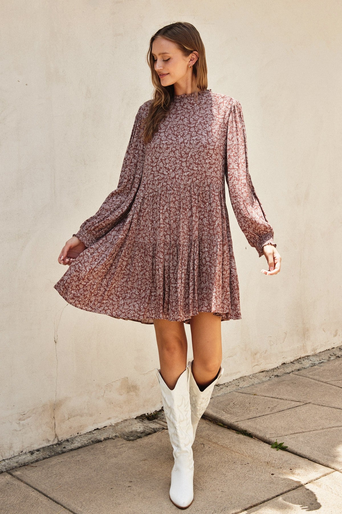 woman wearing a floral long sleeve dress in dusty rose with a pleated skirt and white cowboy boots