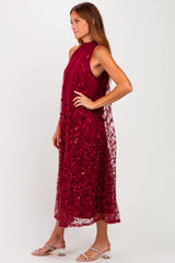 woman wearing a burgundy sleeveless maxi dress with floral embroidery and a sheer overlay