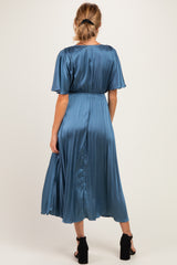 woman wearing a blue satin maternity maxi dress with flutter sleeves and a cinched waist, showing a baby bump