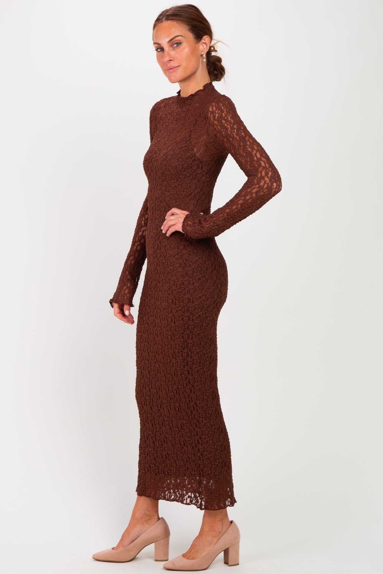 woman wearing a brown long sleeve knitted dress with a fitted silhouette and side slit, paired with beige heels