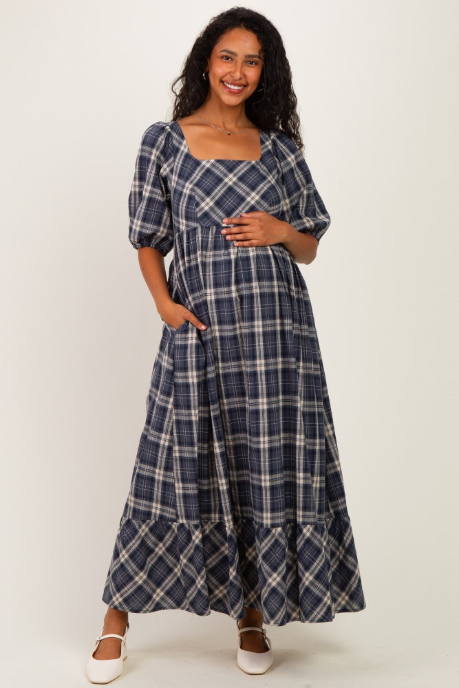 woman wearing a navy plaid maternity maxi dress with puff sleeves and pockets, holding her baby bump