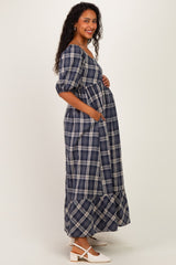 woman wearing a navy blue and cream plaid maternity maxi dress with puff sleeves and pockets, showing her baby bump