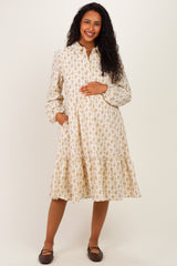 woman wearing a cream floral maternity dress with a tiered skirt and pockets, holding her baby bump