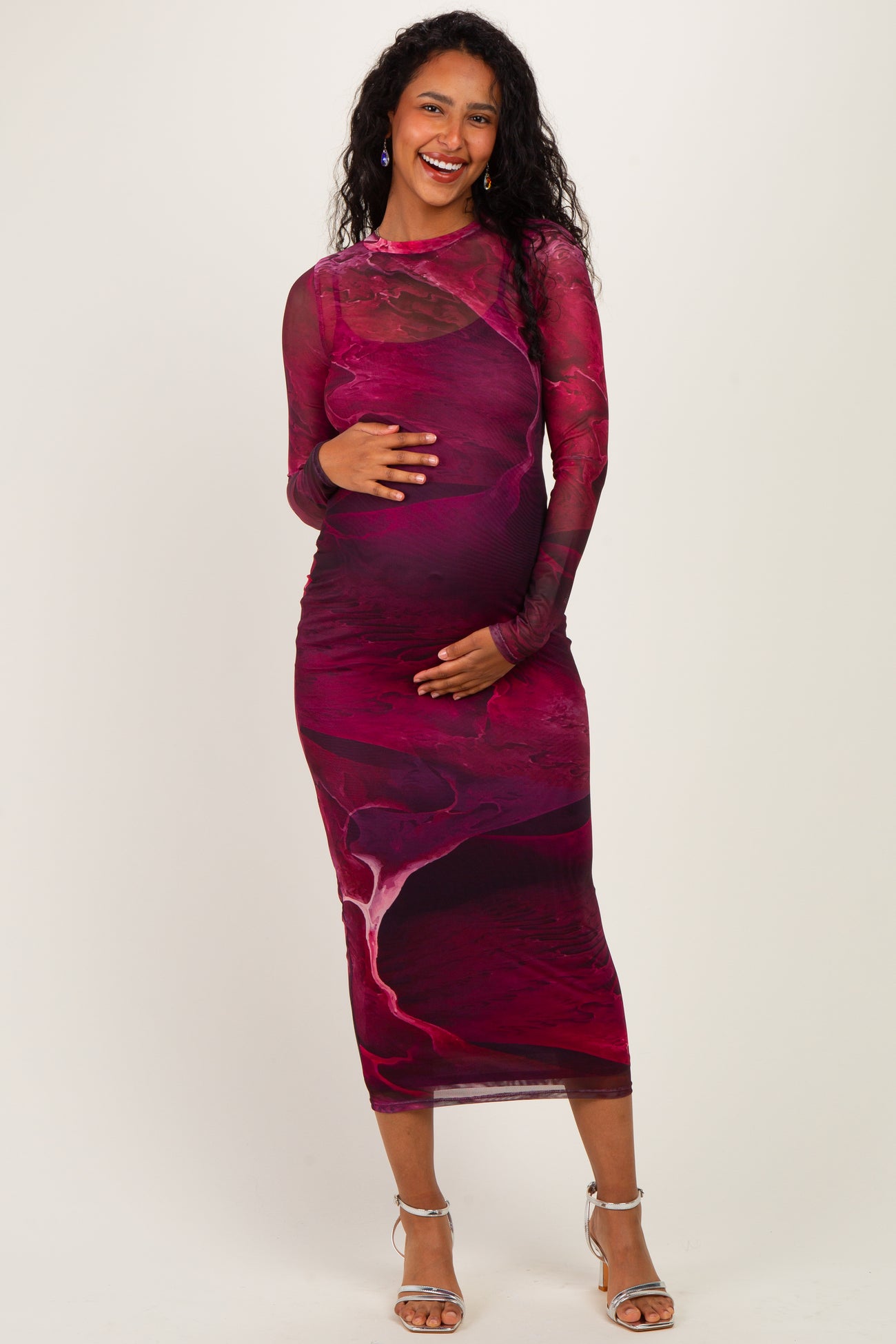 woman wearing a long sleeve maternity dress in a red and burgundy abstract design, gently holding her baby bump