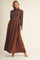 woman wearing a brown ribbed sweater and a flowing brown maxi skirt, standing elegantly against a neutral background