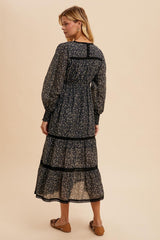 woman wearing a black floral maxi dress with long sleeves and ruffle details, shown from the back