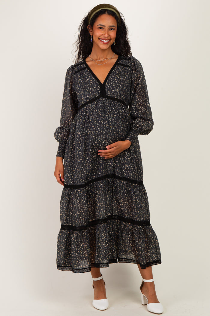 woman wearing a black floral maternity maxi dress with puff sleeves and a baby bump, smiling at the camera