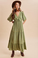 woman wearing a green maxi dress with puff sleeves and a tie front, styled with a wide-brim hat and brown ankle boots