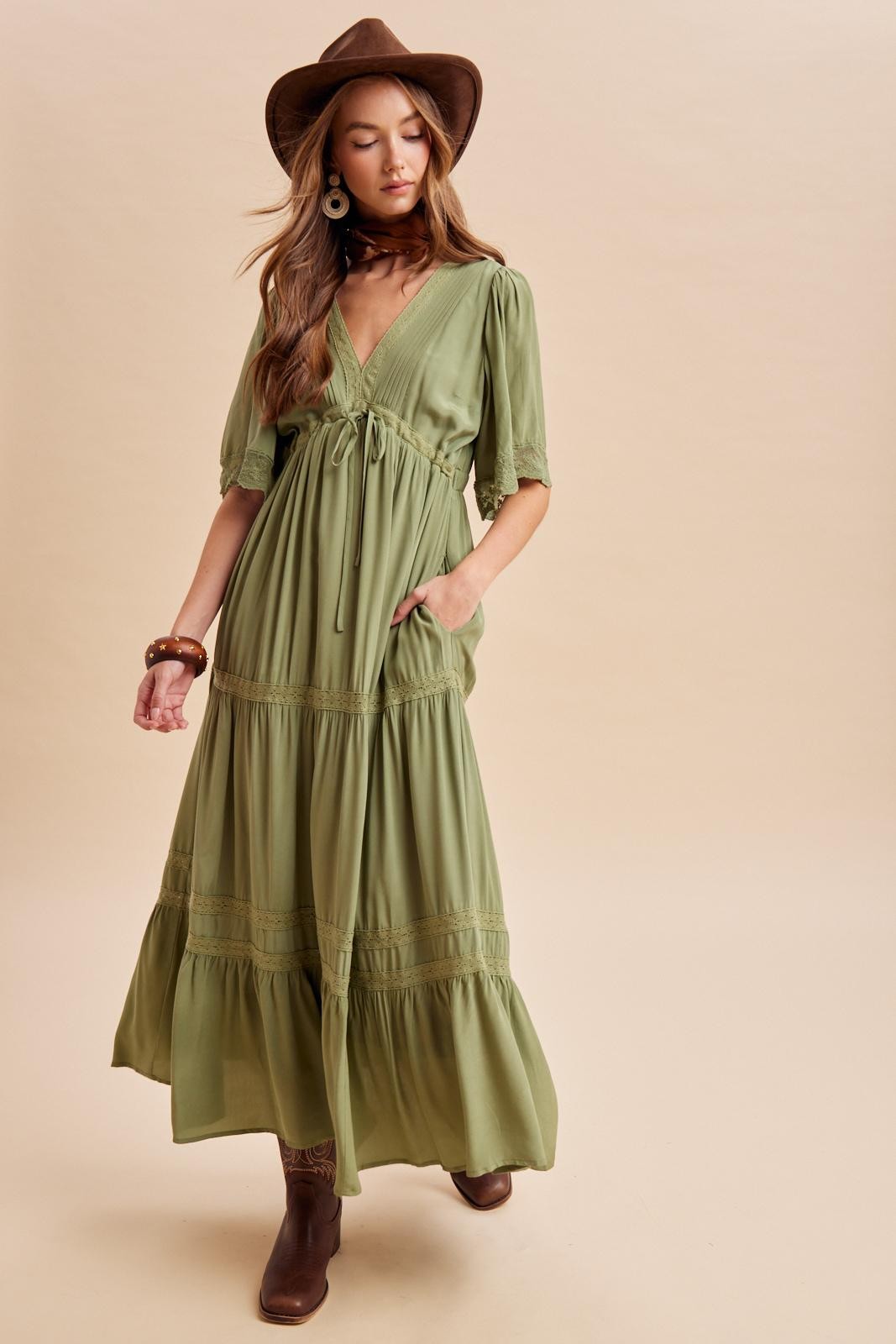 woman wearing a green maxi dress with short puff sleeves, a v-neck, and a tied waist detail, paired with a brown hat