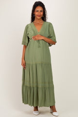 woman wearing a light green maternity maxi dress with short sleeves and lace trim details, posing with a relaxed smile
