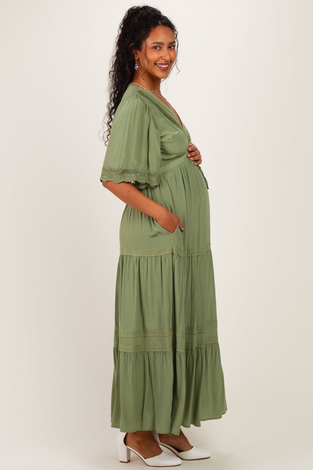 woman wearing a sage green maternity maxi dress with flutter sleeves and pockets, showing her baby bump