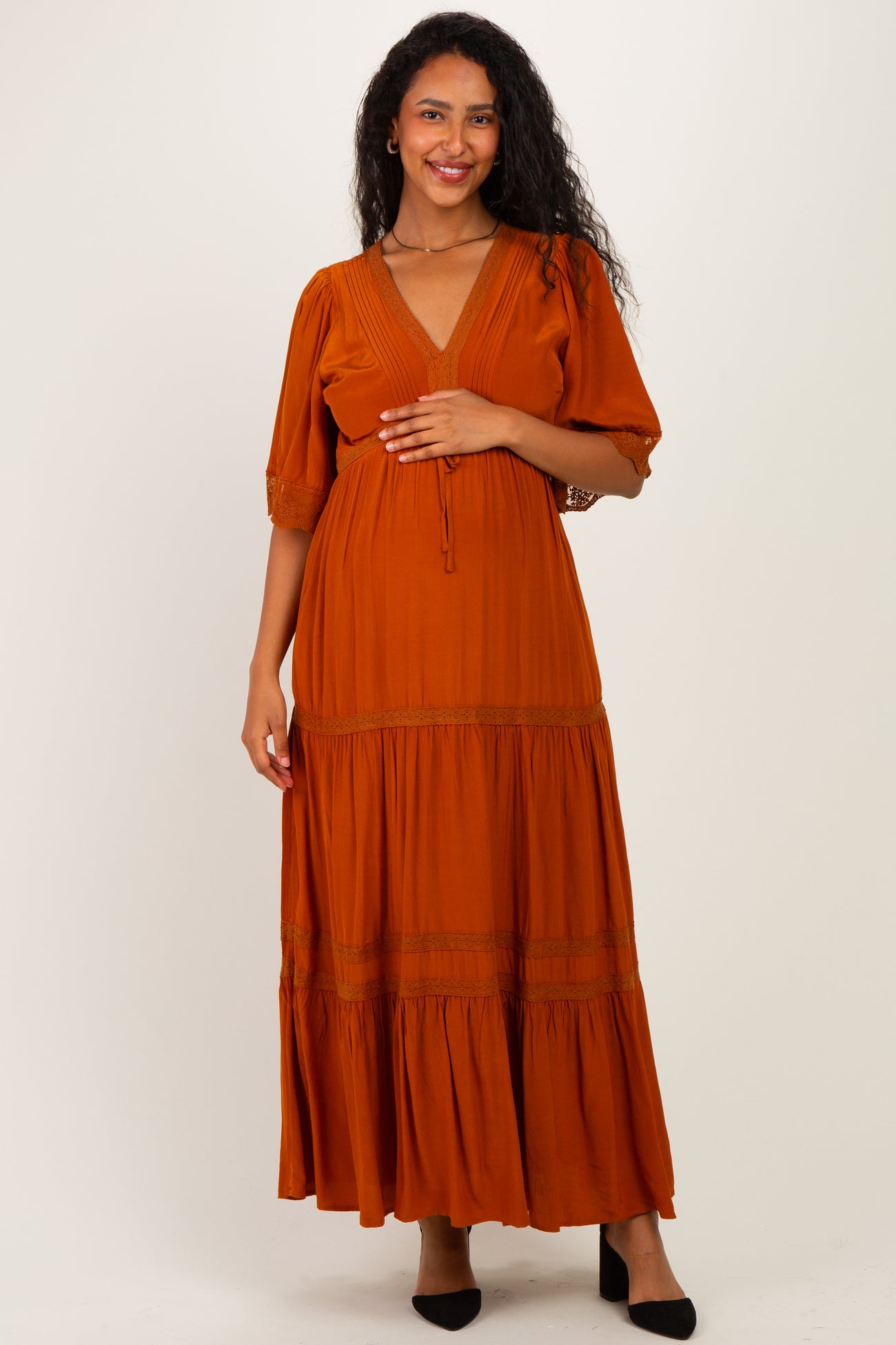 woman wearing an orange maternity maxi dress with puff sleeves and a v-neck, holding her baby bump