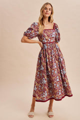 woman wearing a maroon floral midi dress with puff sleeves and a square neckline, standing in a relaxed pose