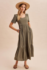 woman wearing a short sleeve olive green maxi dress with pockets and a tiered skirt, styled with a wide-brim hat