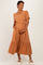 woman wearing a rust colored maternity dress with puff sleeves and a tiered skirt, gently cradling her baby bump
