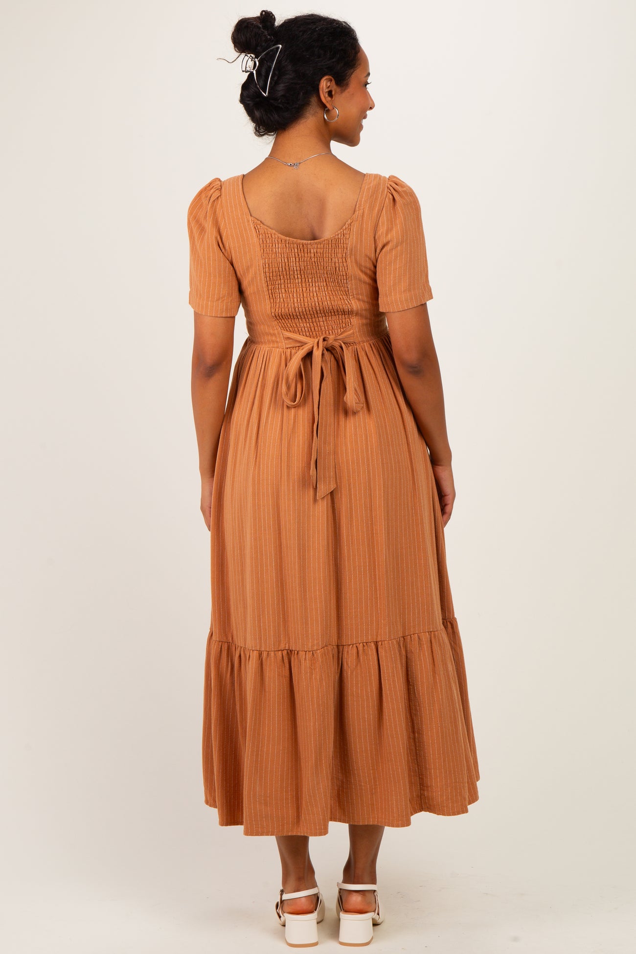 woman wearing a rust-colored maternity dress with short puff sleeves and a tie waist, featuring a tiered skirt