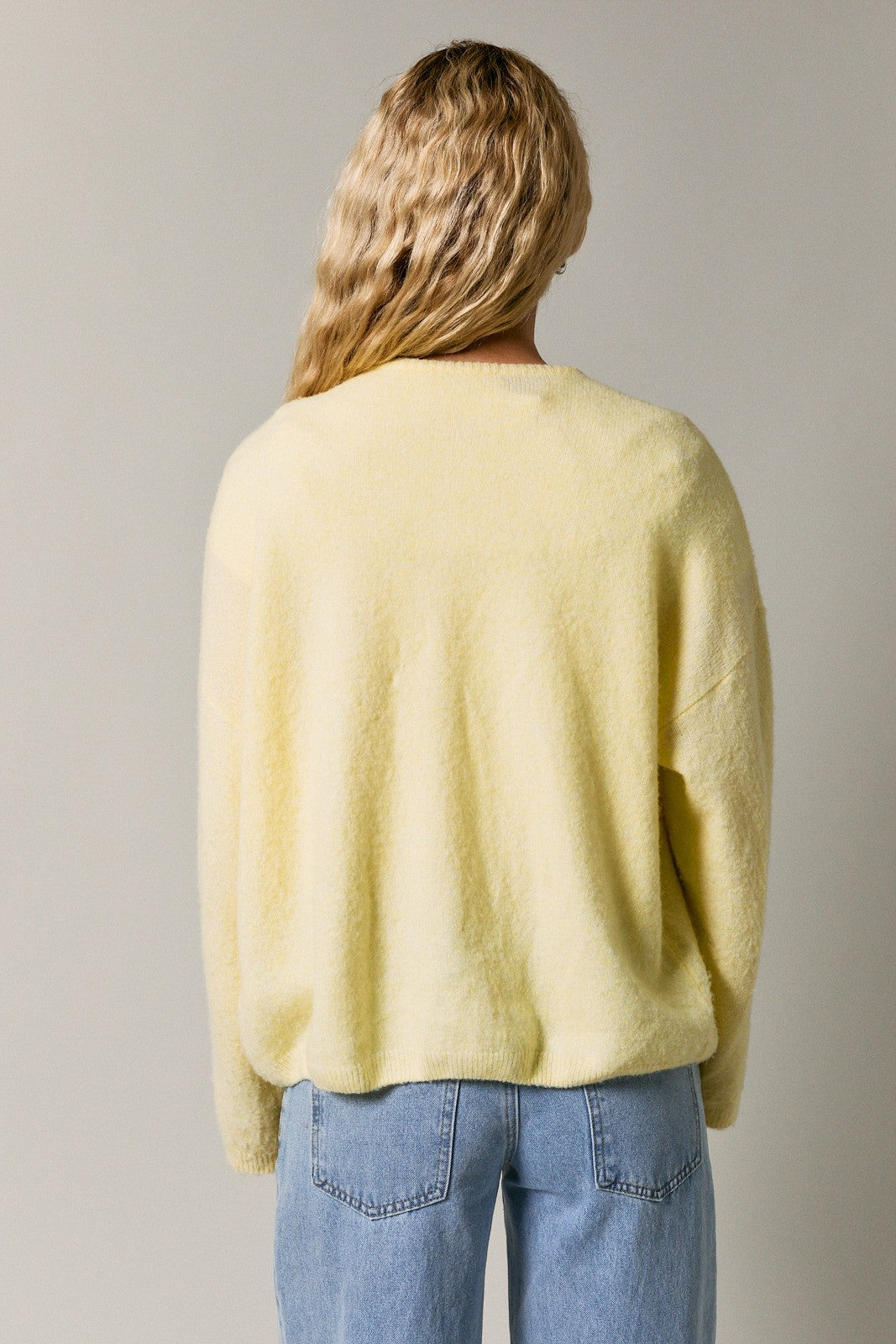 woman wearing a soft yellow oversized sweater seen from the back, paired with light blue jeans
