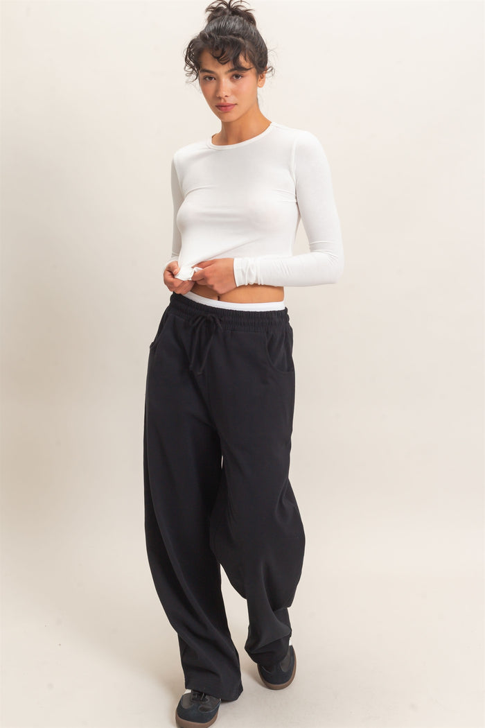woman wearing a white long sleeve top and black wide-leg sweatpants with pockets