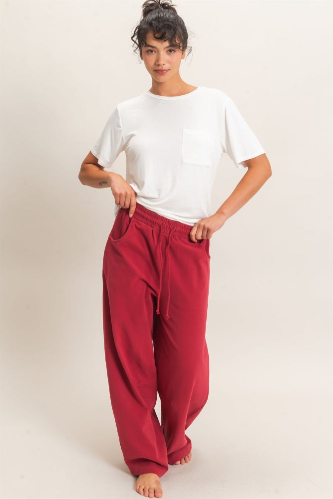 woman wearing a white short sleeve t-shirt and red wide-leg pants, standing with hands in pockets