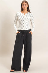 woman wearing a white polka dot long sleeve top and black wide-leg pants with pockets