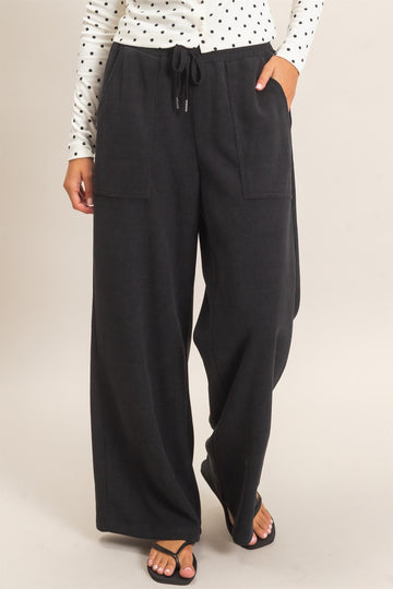 woman wearing black wide-leg lounge pants with side pockets and drawstring waist, styled with a polka dot long sleeve top
