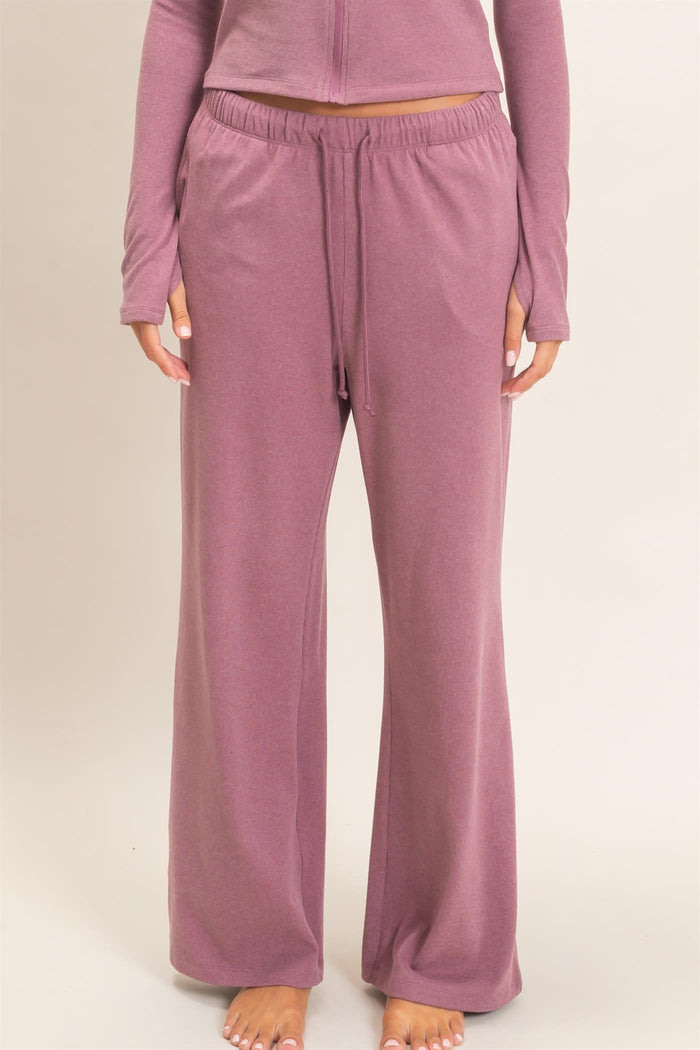 woman wearing a mauve loungewear set with long sleeve top and wide-leg pants, standing barefoot
