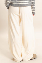 woman wearing white wide-leg pants, standing with her back to the camera, paired with a gray striped sweater