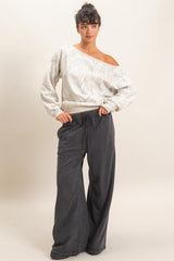woman wearing a light gray off-shoulder sweater with floral print and black wide-leg sweatpants