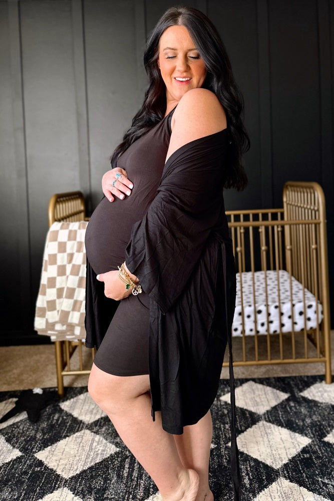 woman wearing a black maternity dress with a matching wrap and holding her baby bump