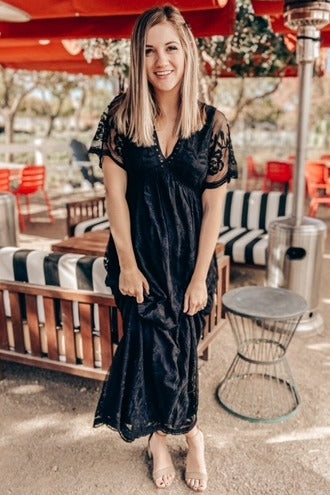 woman wearing a black lace maxi dress with short sleeves, standing outdoors in a casual setting