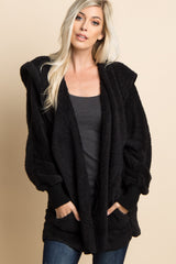 woman wearing a black fluffy oversized jacket over a white crop top against a green background