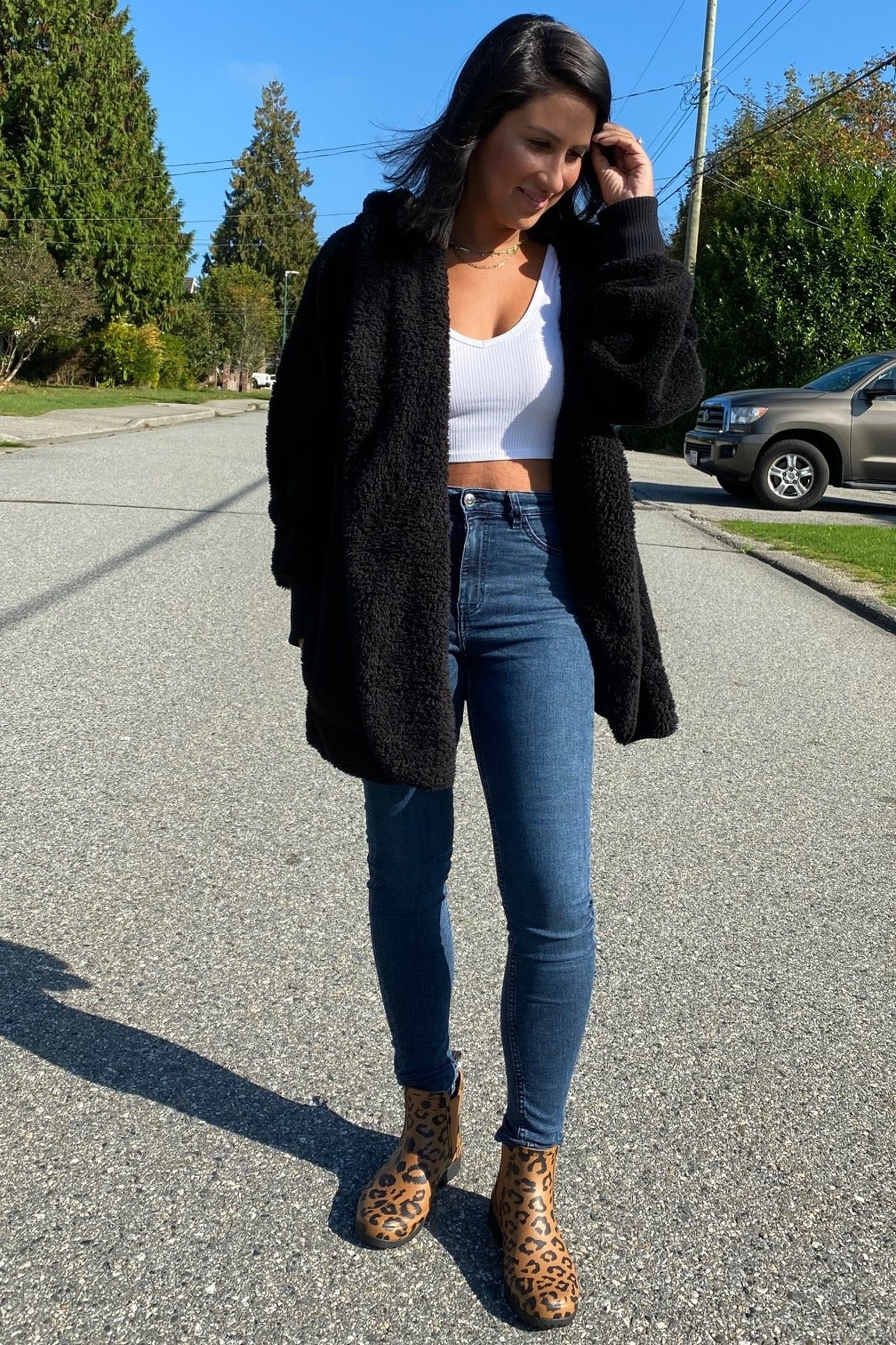 woman wearing a black fuzzy oversized cardigan, white tank top, high-waisted jeans, and leopard print ankle boots