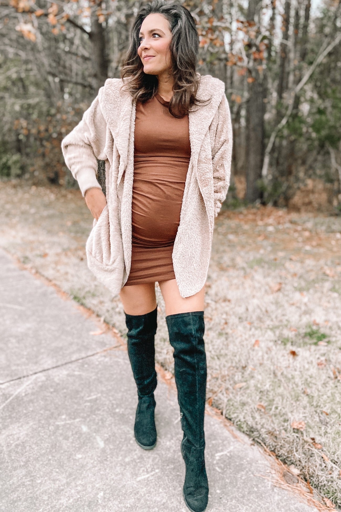 woman wearing a brown bodycon maternity dress and a beige oversized cardigan, showing her baby bump while walking outdoors