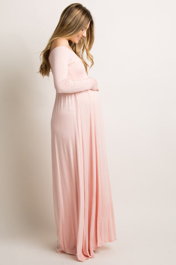 woman wearing a blush pink off-the-shoulder maternity maxi dress and holding her baby bump