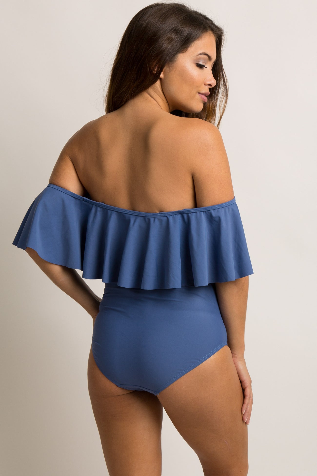 woman wearing a navy blue off-the-shoulder maternity cover-up with white tassels and holding a straw bag while showing her baby bump