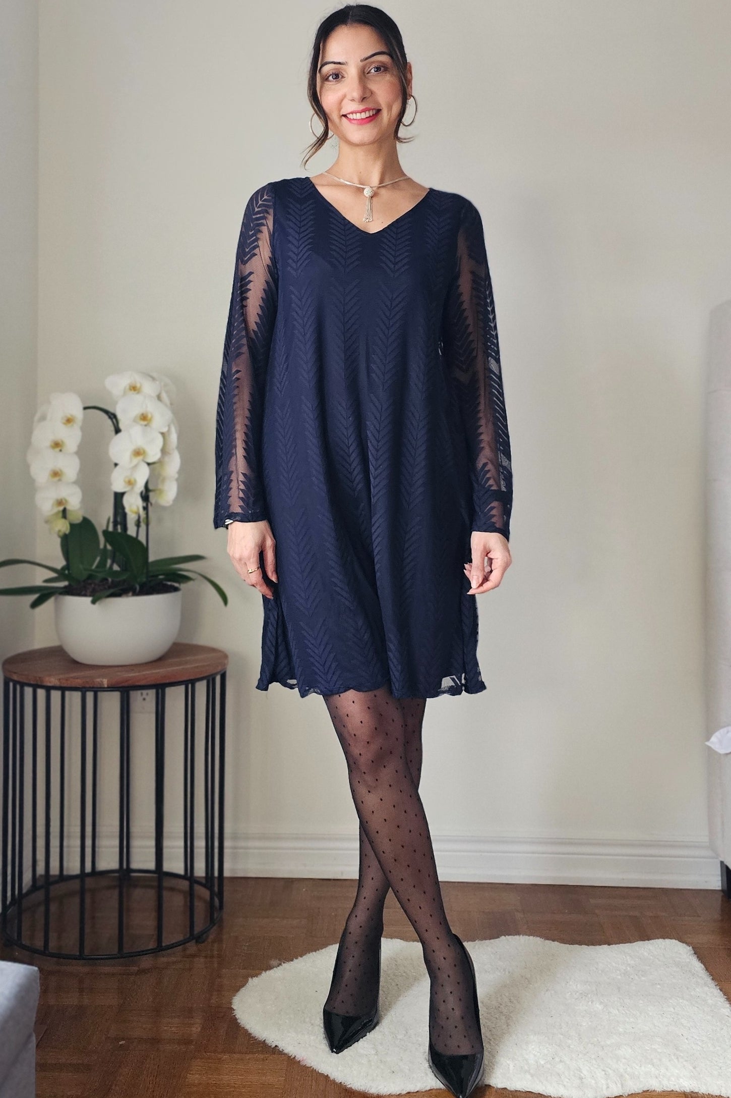 woman wearing a navy blue long sleeve dress with sheer sleeves and a v-neckline, paired with polka dot tights and heels