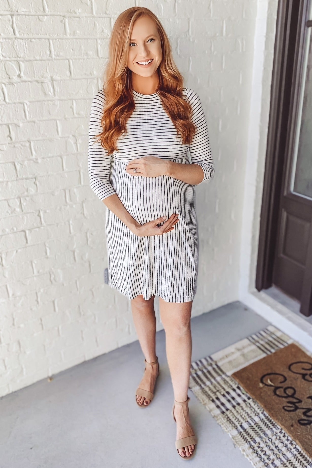 woman wearing a striped maternity dress and gently holding her baby bump