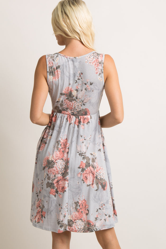Back view of a blonde woman wearing a sleeveless light blue floral print maternity dress with pink roses