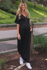 woman wearing a black maternity maxi dress with ruffled sleeves and buttons, showing her baby bump while standing outdoors
